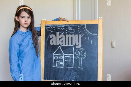 the girl drew a house and the sun with chalk on the Board, so she learns to draw Stock Photo