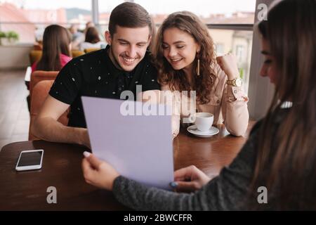 Happy couple in cafe meet with bussines woman. Woman show to man and woman something on documents. Stock Photo