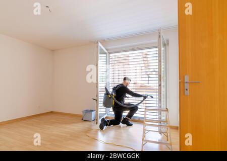 young male professional cleaner vacuuming dirty window blinds and cleaning htem thoroughly Stock Photo