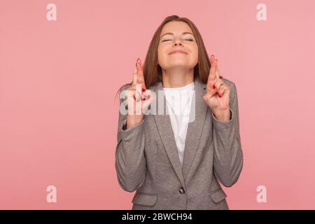 I am lucky, dreams come true! Portrait of optimistic young woman in business suit making wish and holding fingers crossed for good luck, hoping for su Stock Photo