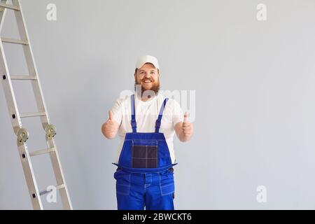 Optimistic male builder in uniform near metal ladder at gray background Stock Photo