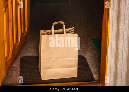 Contactless delivery service during quarantine. Carton craft bag delivered and left outside at entrance door. Stock Photo