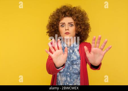 No, it's scary! Portrait of frightened shocked woman with curly hair in casual outfit raising hands in fear, looking horrified and panicking, hiding f Stock Photo