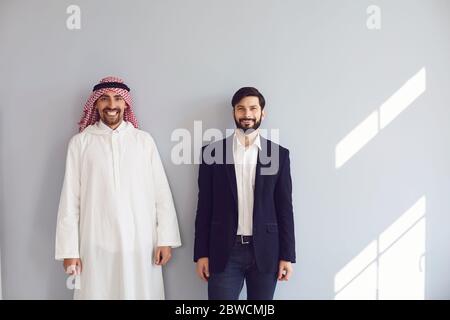 Arab and european businessmen stand smiling at the gray background. Stock Photo