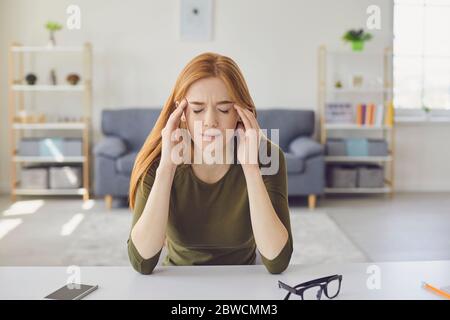 Beautiful girl feeling unwell, calling her doctor online from home. Young woman on video chat with health care provider.Headache. Stock Photo