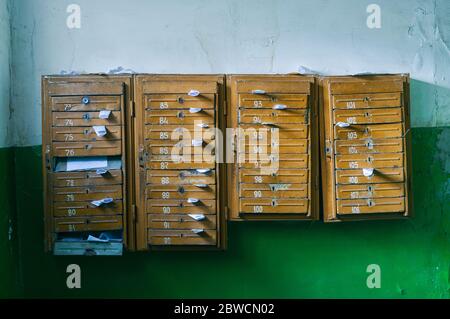 Old mailboxes in the entrance hall of a residential house filled with white paper flyers. Mass mailing concept. Stock Photo