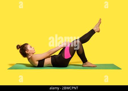 Motivated fitness woman with hair bun in yoga pants training on gym mat, reaching hands to feet stretching muscles, warming up with flexibility exerci Stock Photo