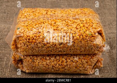 Yellow split peas in a cellophane bag on a background of coarse-textured burlap. Traditional grains for making soups and porridges. Close up Stock Photo