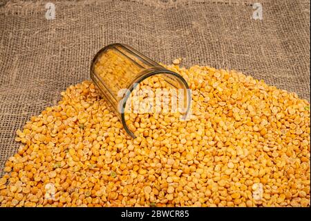 Yellow split peas in a cut glass and grits scattered on a background of coarse-textured burlap. Traditional cereals for making soups and porridge. Clo Stock Photo