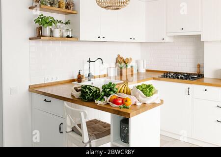 Fresh vegetables and fruits in eco cotton reusable bags on wooden table in the kitchen. zero waste shopping concept. Sustainable living Stock Photo