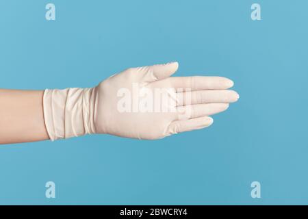 Profile side view closeup of human hand in white surgical gloves giving hand to greeting or touching. indoor, studio shot, isolated on blue background Stock Photo