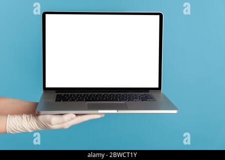 Profile side view closeup of human hand in white surgical gloves holding computer laptop and showing empty copy space on monitor screen. indoor, studi Stock Photo