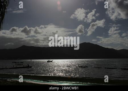 backlighting of a shore with mountains, boats, and people Stock Photo