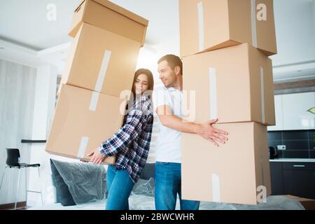 Young couple carrying many cardboard boxes one by one at new home. Moving house. Stock Photo