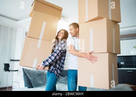 Young couple carrying many cardboard boxes one by one at new home. Moving house. Stock Photo