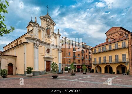 Catholic church and historic house on small town square under cloudy sky in Alba, Piedmont, Northern Italy. Stock Photo