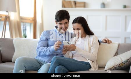Happy couple rest on sofa using smartphone Stock Photo
