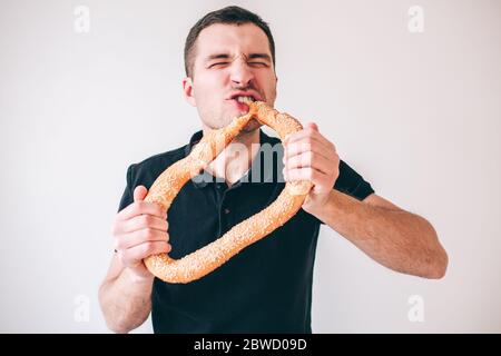 Young man isolated over background. Picture of guy holding big round bun and biting it with pleasure. Stand alone in studio and posing. Stock Photo