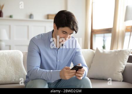 Smiling young man using modern smartphone at home Stock Photo