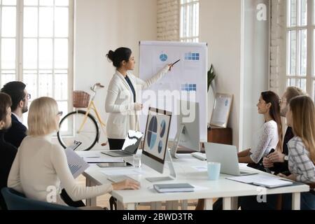 Focused colleagues sitting at shared table, listening to indian speaker Stock Photo