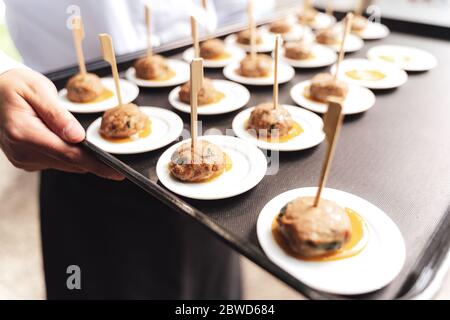 Roasted meatballs served on small white plates. Male hands holding black tray. Selective focus. Celebration, birthday, party, wedding concept. Stock Photo