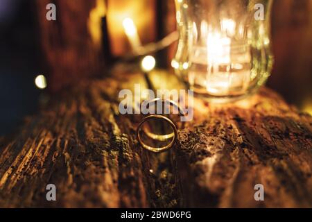 Pair of marriage rings standing on old piece of wood. Decorative light in background. Toned to warm colors. Stock Photo