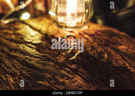 Couple of wedding rings standing on old wooden surface close up. Decorative glass light in background. Toned to warm colors. Stock Photo