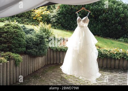 Bride's wedding gown on hanger on fresh air. Green outdoor park background. Wedding day concept. Stock Photo