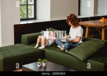 redhead freelancer using laptop near cute daughter with digital tablet Stock Photo