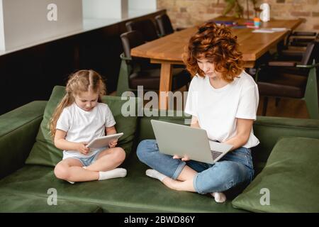 redhead freelancer using laptop near daughter with digital tablet Stock Photo