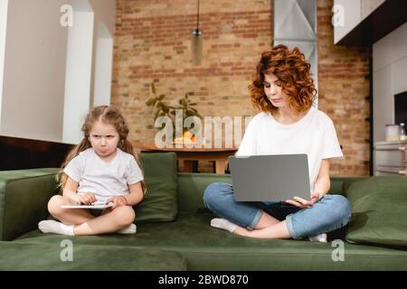 redhead freelancer using laptop near sad daughter with digital tablet Stock Photo