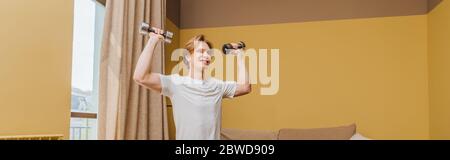 panoramic crop of happy young man exercising with dumbbells in living room, end of quarantine concept Stock Photo