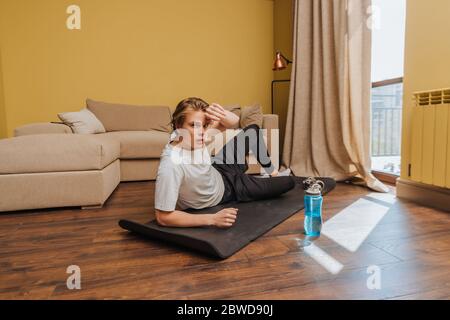 tired man lying on fitness mat near sports bottle with water, end of quarantine concept Stock Photo