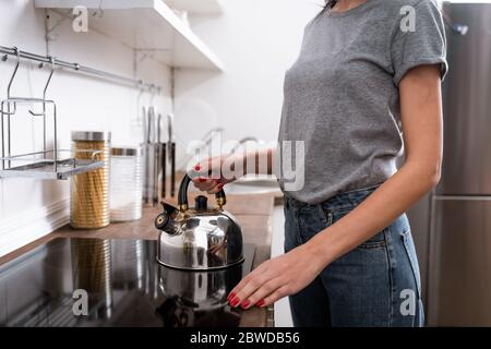 cropped view of woman touching teapot on electric stove in kitchen Stock Photo