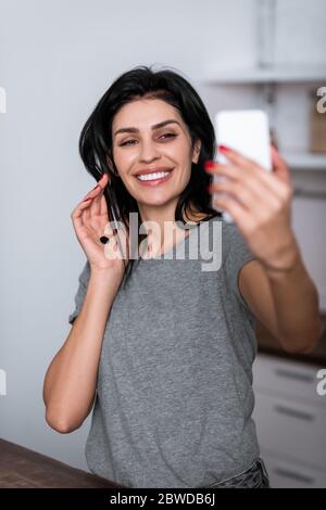 selective focus of smiling woman with bruise on face and black dot on palm taking selfie, domestic violence concept Stock Photo