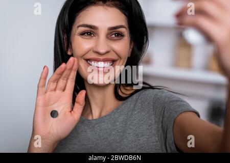 selective focus of smiling woman with bruise on face and black dot on palm taking selfie at home, domestic violence concept Stock Photo