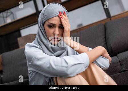 Depression concept. Upset muslim woman in hijab crying on sofa at home ...