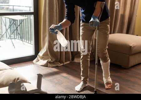 Cropped view of man with broken leg using detergent while holding crutch at home Stock Photo
