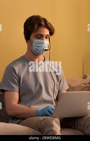 Man in medical mask and latex glove using headset and laptop at home Stock Photo