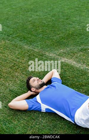 professional soccer player in blue and white uniform lying on football pitch at stadium Stock Photo