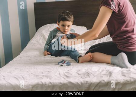 partial view of woman dressing adorable son while sitting on bed Stock Photo