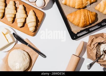 top view of raw and baked croissants on baking tray near ingredients on white background Stock Photo