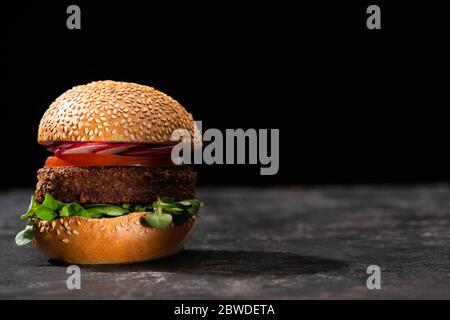 tasty vegan burger with microgreens, radish and tomato served on textured surface isolated on black Stock Photo