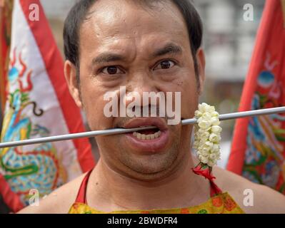 Thai Chinese Taoist devotee pierces his left cheek with a long steel pin during the Phuket Vegetarian Festival (Nine Emperor Gods Festival). Stock Photo