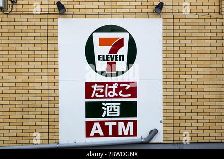 7-Eleven Convenience Store Sign against Yellow Brick Wall in Tokyo, Japan with Japanese letters that read “Seven Eleven” and “ATM” Stock Photo