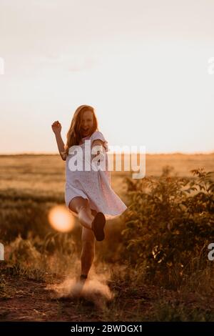 Young beautiful woman making dust with her foot and screaming in the wheat orange field on a sunny summer day. Going crazy. Feeling free and happy. Mi Stock Photo