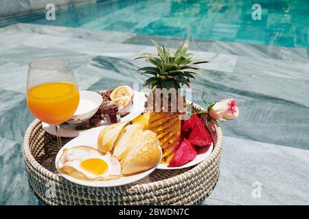 Breakfast consisting of friend egg, white bread and tasty sweet fruits on big wicker tray Stock Photo