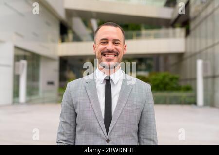 Happy Hispanic bald bearded businessman smiling in the city outdoors Stock Photo