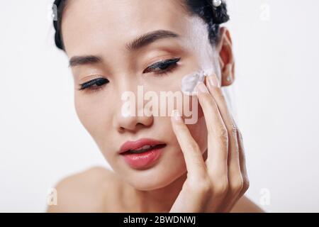 Beautiful young Vietnamese woman applying moisturizer on her face Stock Photo