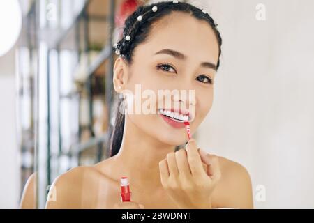Beautiful young Vietnamese woman applying matte red liquid lipstick Stock Photo